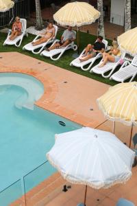 un grupo de personas sentadas en sillas de césped bajo sombrillas junto a una piscina en Abode Mooloolaba, Backpackers & Motel rooms, en Mooloolaba