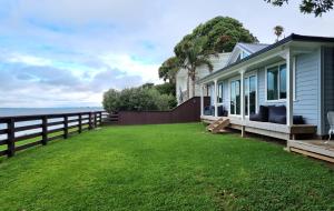 uma casa com um grande quintal ao lado de uma cerca em Red Rock Cottage, beachfront luxury em Clarks Beach