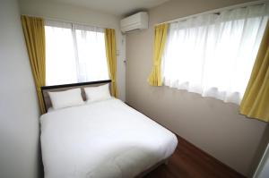 uma cama num quarto com duas janelas em Plage Garden Place　A-101 em Miyako Island