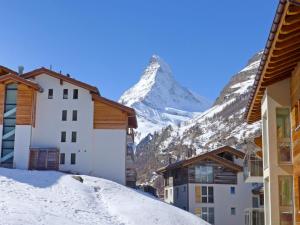 a snow covered mountain in the distance behind buildings at Apartment Grillon-3 by Interhome in Zermatt