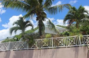 a white fence in front of a house with palm trees at La Belle Étoile - Jolie villa créole Trois Ilets plage in Les Trois-Îlets