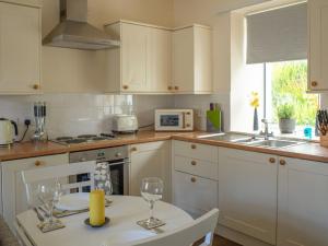 a kitchen with white cabinets and a table with wine glasses at Apartment Flat 2 Keeper's Cottage by Interhome in Stenscholl