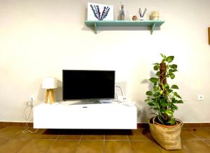 - une télévision sur une table blanche dans une chambre avec une plante dans l'établissement MyChoice Costa Atlántica by Bossh Apartments, à Rota