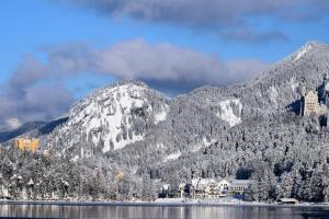 a mountain covered in snow next to a lake at AMERON Neuschwanstein Alpsee Resort & Spa in Schwangau