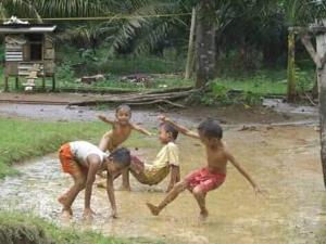 three children playing in the mud in the rain at Tour & Travel Guide in Bukit Lawang