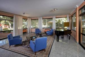 a living room with a grand piano and blue chairs at Park Hotel I Lecci in San Vincenzo