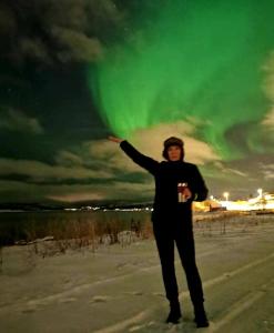 a woman standing in the snow under a green sky at Aurora rooms for rent nr3 we are doing Northen Lights trip, Reaindear trip and Sommaroy Fjord trips in Tromsø