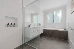 a white bathroom with a shower and a tub and a sink at The Quarterdeck in Callala Bay