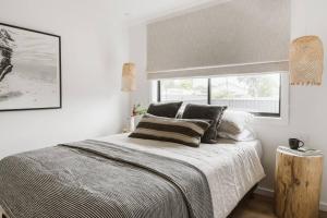 a white bedroom with a large bed and a window at The Lull Culburra in Culburra Beach