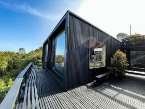 a black house with a large window on a deck at El Coo Lodge in Queilén
