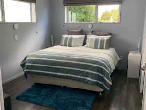um quarto com uma cama com um cobertor listrado e duas janelas em Mason lane Apartment em Whangarei