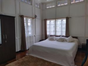 1 dormitorio con 1 cama con sábanas blancas y ventanas en Casa Encanto Homestay, en Shillong