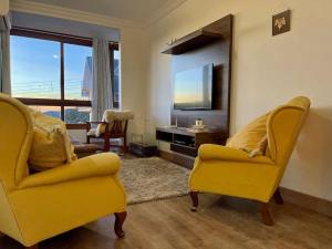 Sala de estar con 2 sillas amarillas y TV en MARAVILHOSO Apartamento VISTA DO VALE e 2 dorm, en Gramado