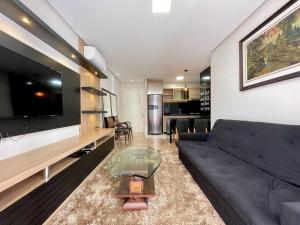 sala de estar con sofá negro y TV en Apartamentos Loft One no CENTRO by Achei Gramado, en Gramado
