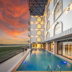 a building with a swimming pool with a sunset in the background at Eastin Hotel Vientiane in Vientiane
