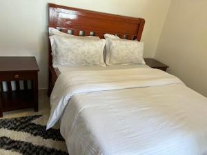 une chambre avec un lit blanc avec une tête de lit en bois dans l'établissement ArushaWest, à Arusha