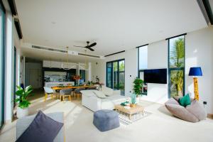 una sala de estar abierta con muebles blancos y ventanas grandes. en Perolas Villas Resort Powered by ASTON, en Phan Thiet