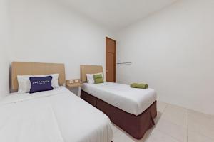 two beds in a room with white walls at Urbanview Hotel Cozy Samarinda by RedDoorz in Samarinda
