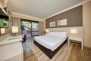a bedroom with a bed and a desk and a window at Park Hotel I Lecci in San Vincenzo
