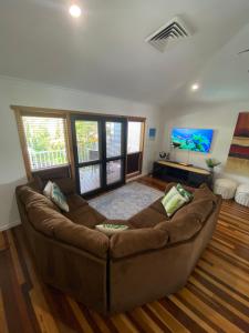 a living room with a brown couch and a flat screen tv at Luxury Top Floor Sunset Villa in Noosaville
