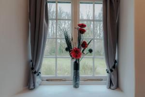 Un jarrón con flores rojas sentado en una ventana en Sheviock Barton Bed & Breakfast en Sheviock