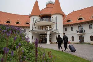 two people walking in front of a building with luggage at Hungarikum Hotel in Lakitelek