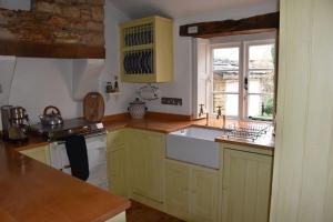 cocina con armarios amarillos y fregadero blanco en Riverside Cottage, en Lower Slaughter