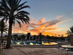 - une piscine avec un palmier et un coucher de soleil dans l'établissement Les Jardins d Amizmiz, à Marrakech