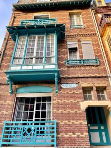 un grand bâtiment en briques avec des fenêtres et des balcons bleus dans l'établissement La Batelière, appartement mer avec patio privé, à Mers-les-Bains