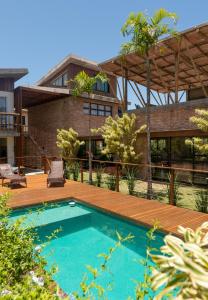 a swimming pool with a wooden deck and a house at Pousada Rosa Tropicalia in Praia do Rosa
