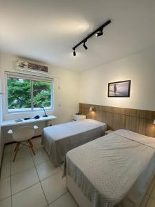 1 dormitorio con 2 camas, escritorio y ventana en Apartamento Completo em Jurerê Florianópolis, en Florianópolis
