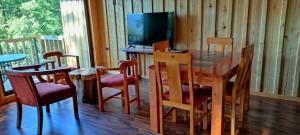 comedor con mesa, sillas y TV en Huallerupe Lodge, en Melipeuco