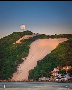 a moonrise over a sandy beach with a hill at Bicalho Flat beira mar - Hotel PontaNegraBeach in Natal