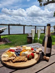 Serenity by the Lake - Romantic Waterfront Couple's Getaway في Marks Point: زجاجة من النبيذ وصحن من الطعام وكؤوس النبيذ