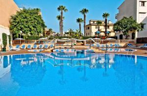 une grande piscine bleue avec des chaises et des palmiers dans l'établissement BQ Can Picafort Hotel, à Can Picafort