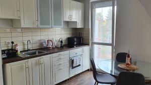 cocina con armarios blancos, mesa y ventana en Levendula Apartman Bükkszentkereszt, en Bükkszentkereszt