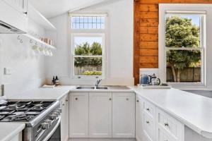 cocina blanca con fregadero y 2 ventanas en Balmoral Cottage - beach escape, en Kingston Beach