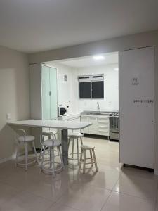 uma grande cozinha branca com uma mesa e bancos em Férias na Praia dos Ingleses em Florianópolis