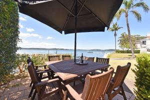 un tavolo in legno con sedie e ombrellone di Baywatch Waterfront Lake Retreat with Private Jetty at Silverwater Lake Macqaurie a Bonnells Bay