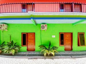a green building with wooden doors and palm trees in front at Papilo House near Stasiun Nganjuk Mitra RedDoorz in Nganjuk