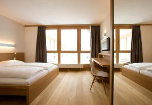 Schlafzimmer mit einem Bett und einem Schreibtisch mit einem TV in der Unterkunft Hotel Manggei Designhotel Obertauern in Obertauern