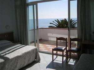 a bedroom with a bed and two chairs and a balcony at Hotel Corallo in Finale Ligure