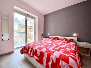 a red and white bed in a room with a window at Central Private En-Suite with Balcony in shared residence in Tal-Pietà