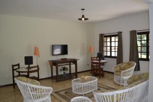 ein Wohnzimmer mit weißen Stühlen und einem TV in der Unterkunft Pousada das Rosas in Miguel Pereira