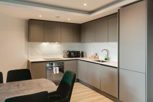 cocina con armarios grises, mesa y sillas en Brentford Apartments by Charles Hope en Brentford