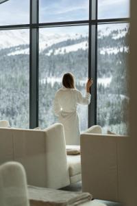 Eine Frau, die aus dem Fenster schaut auf einen verschneiten Berg. in der Unterkunft URSPRUNG Panorama Hotel Königsleiten in Königsleiten