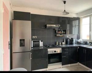 een keuken met zwarte kasten en een roestvrijstalen koelkast bij Massi'z in Neuilly-sur-Marne