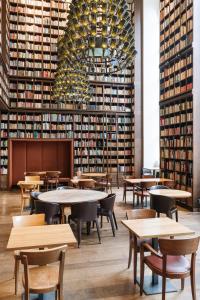 a library with tables and chairs and a large wall of books at B2 Hotel Zürich in Zurich