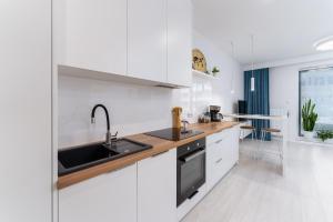 a white kitchen with white cabinets and a sink at Morze-JEZIORO-Las luksusowy apartament Rogowo Pearl in Rogowo