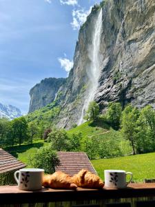 Una mesa con pan y dos tazas de café y una cascada. en Breathtaking Waterfall Apartment nr 3, en Lauterbrunnen